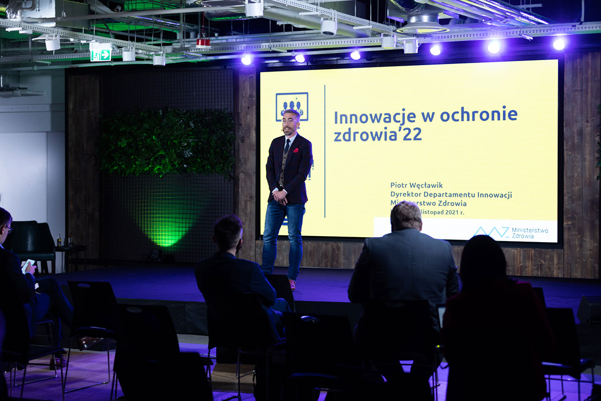 Piotr Węcławik na scenie, w tle slajd Innowacje w ochronie zdrowia'22