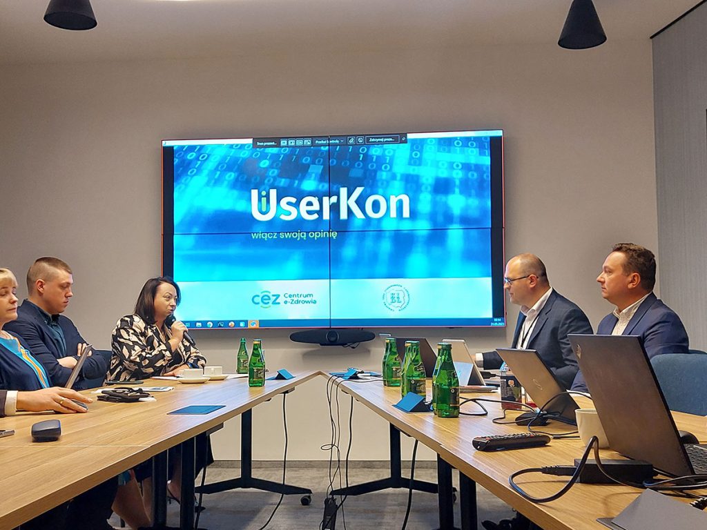 ekran wyśwetlający grafikę userkon i uczestnicy siedzący przy stołach