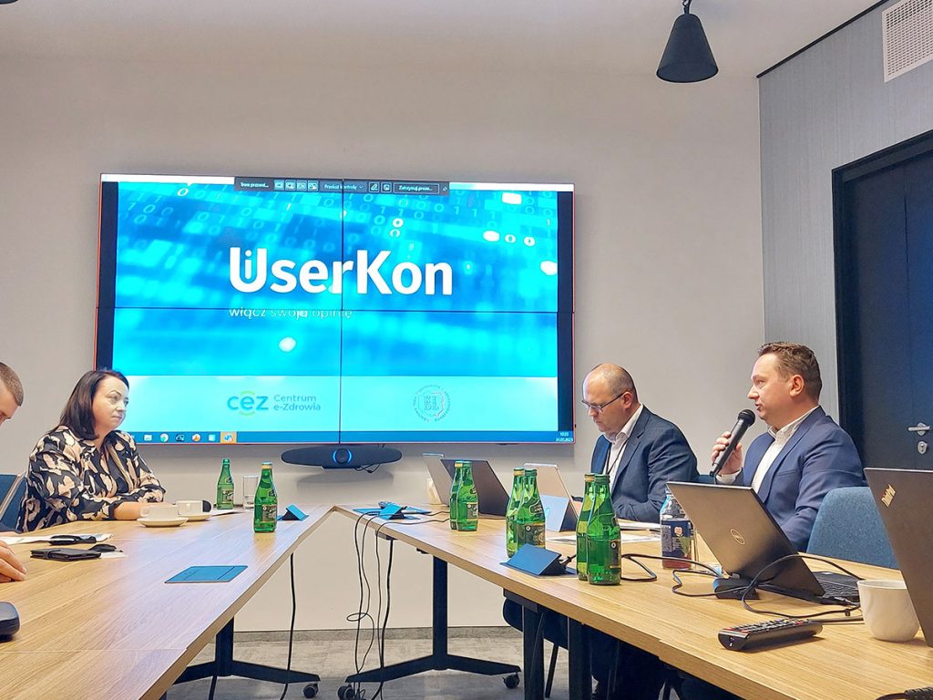 ekran z grafiką userkon i dyrektor kikosicki trzymający mikrofon