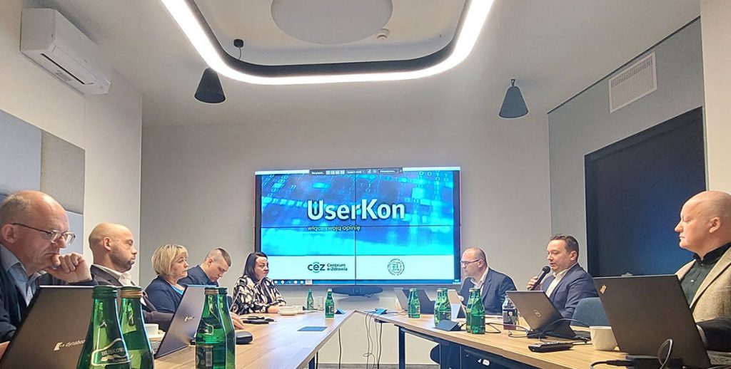 laptopy na stołach a przy nich siedzący uczestnicy spotkania
