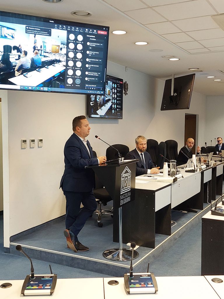 ekran podwieszony do sufitu a pod nim stojący przy mównicy dyrektor Kikosicki
