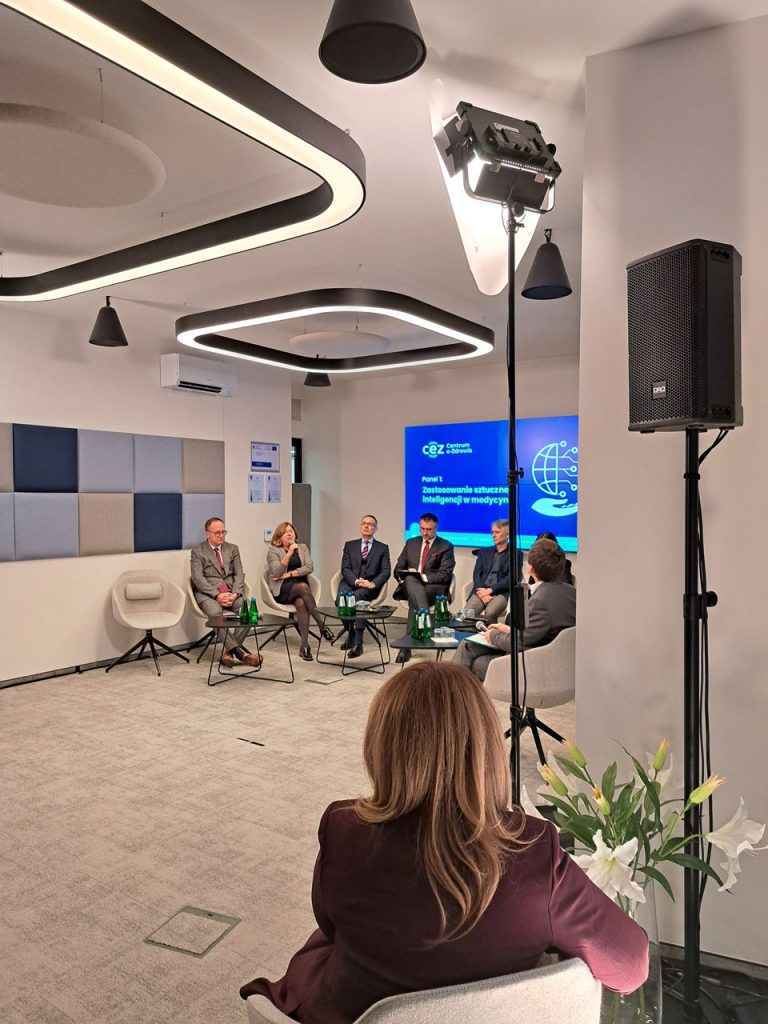 widok na plecy Marty Błędowskiej- prowadzącej konferencję, w dali uczestnicy panelu pierwszego